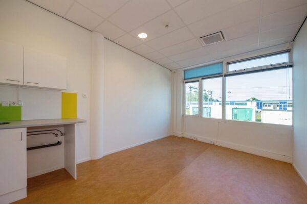 Lichte, lege kamer in het Harriet Freezerhof met een klein keukenblok en uitzicht op spoorlijnen buiten.